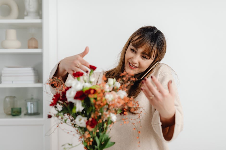 A woman with medium-length brown hair and bangs, smiling warmly as she receives a vibrant floral bouquet. The bouquet features an array of fresh flowers including red roses, white lisianthus, orange p