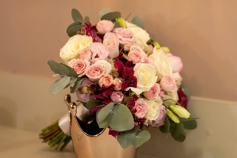 A bouquet arrangement of fresh flowers comprising mainly white and pink roses, interspersed with deep burgundy eustoma and complemented by eucalyptus leaves with rounded, pale green foliage. The flowe